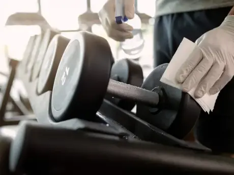 Technician disinfecting a dumbbell during a maintenance visit